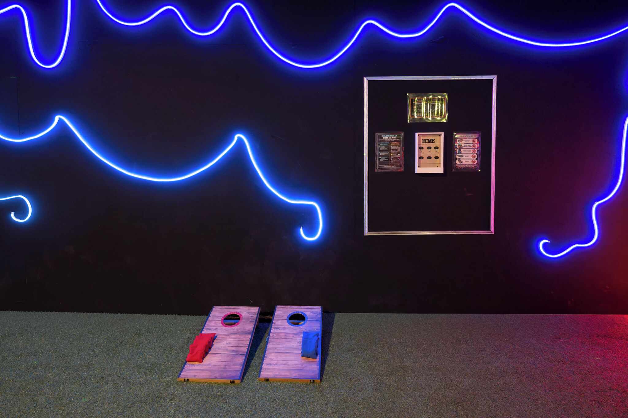 Una stanza con un design luminoso al neon sulla parete, una vetrina incorniciata con oggetti esposti e due pannelli di legno con elementi rossi e blu sul pavimento.