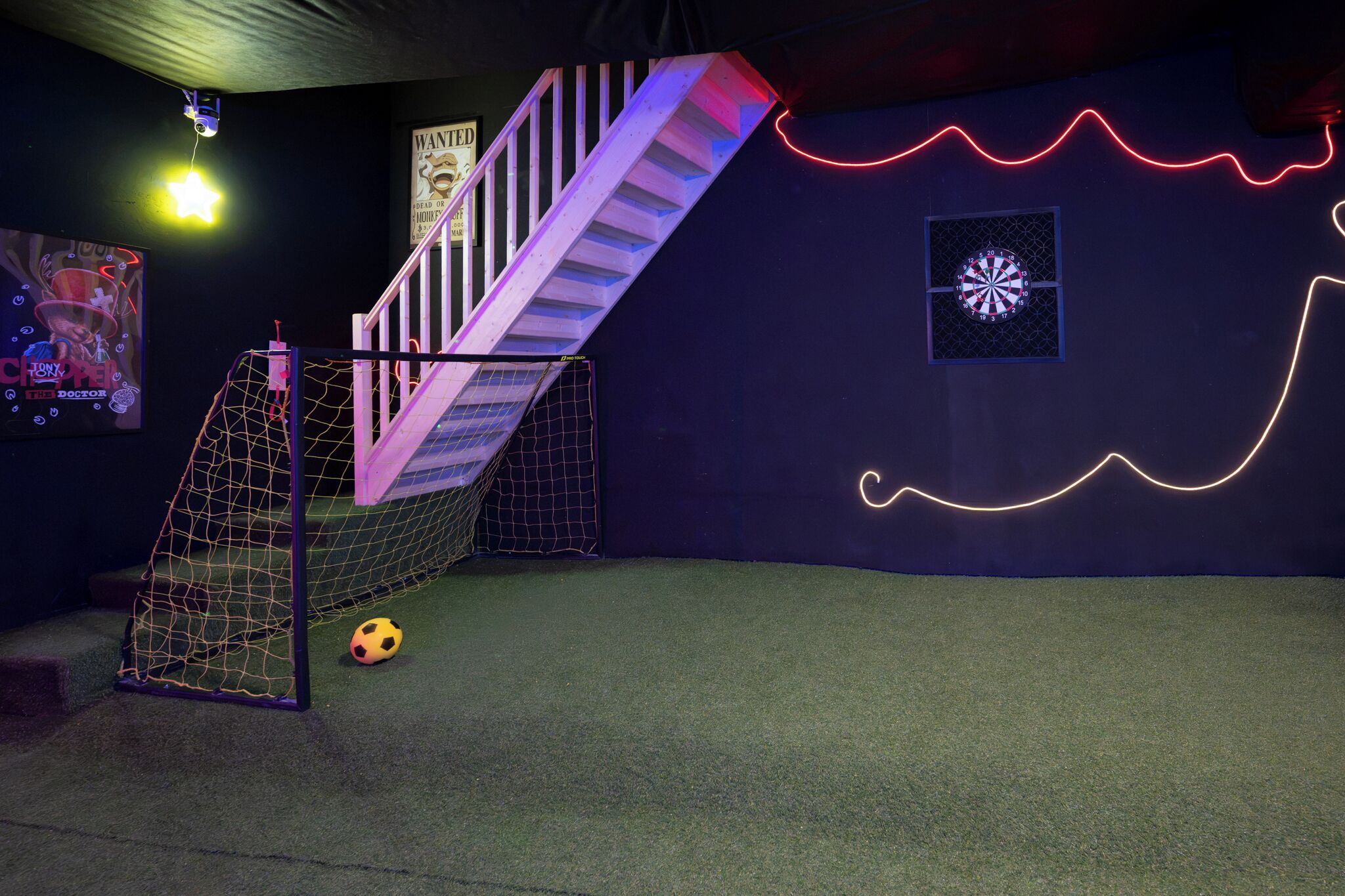 Ein Zimmer mit Fußballtor, einer Treppe und einer Wand mit Neonlichtern.