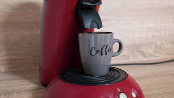 Een rode koffiezetapparaat met een kop koffie erop.