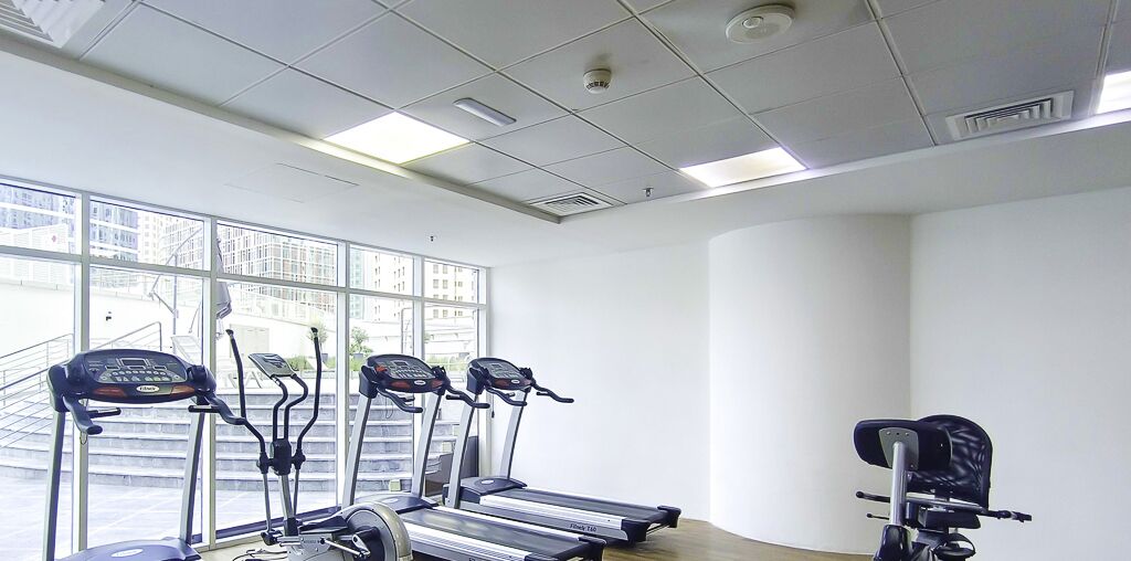 Une salle de sport équipée de tapis de course et d’un vélo d’appartement, de grandes fenêtres offrant une vue sur les bâtiments et un plafond doté d’un éclairage encastré.