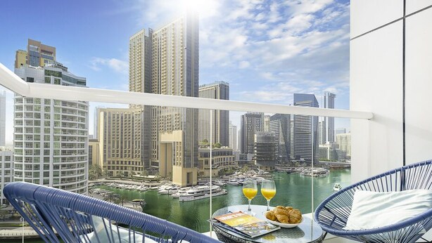 A balcony with a city view, a table with croissants and orange juice, and a wicker chair. - LUX  The Continental Marina Suite (Dubai)