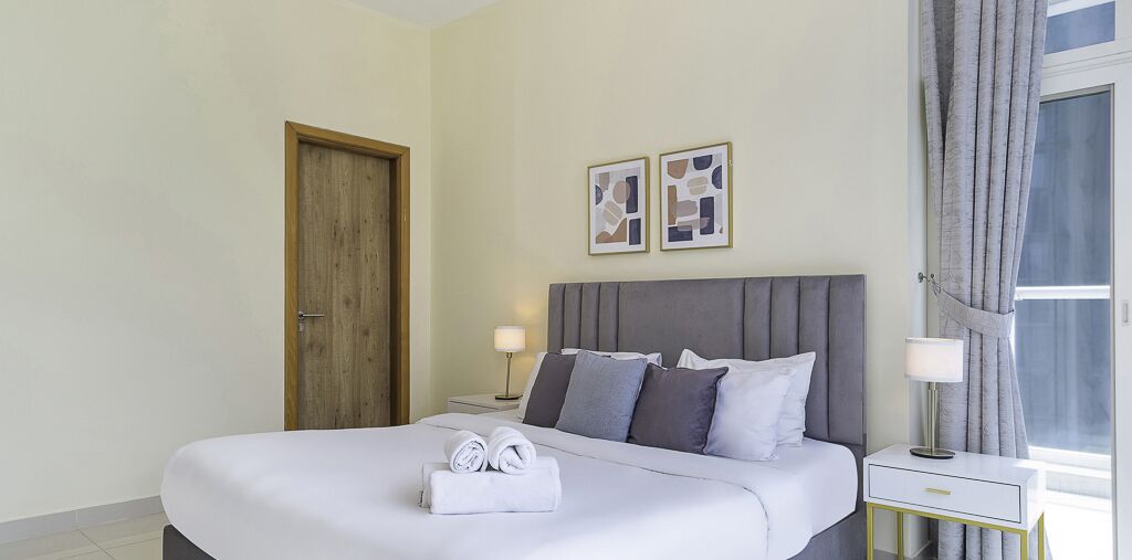 Une chambre d’hôtel avec un grand lit, deux tables de chevet, une porte en bois et deux tableaux encadrés accrochés au mur.