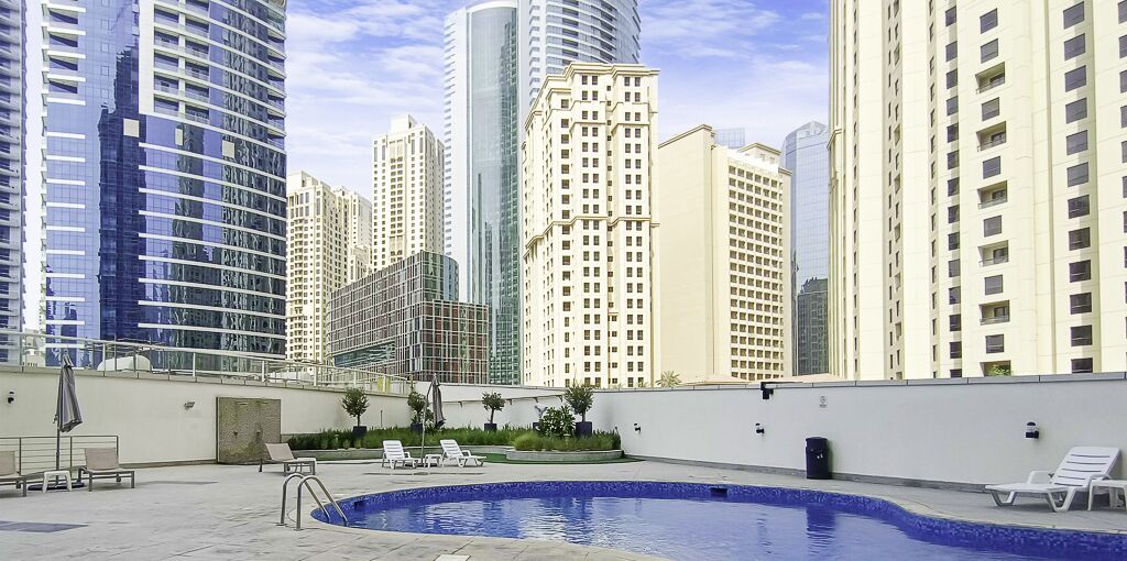 A rooftop pool area with lounge chairs and a swimming pool, surrounded by high-rise buildings.