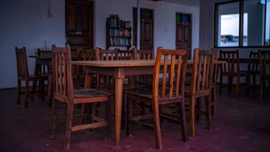 A room with a wooden table surrounded by chairs, a bookshelf, and a window with a view. - Flamingo Guest House (Zanzibar Town)