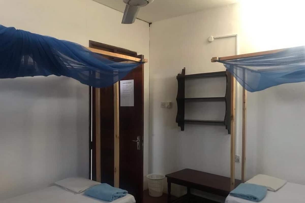 Une chambre de dortoir avec deux lits simples, une petite table, une étagère et une porte.
