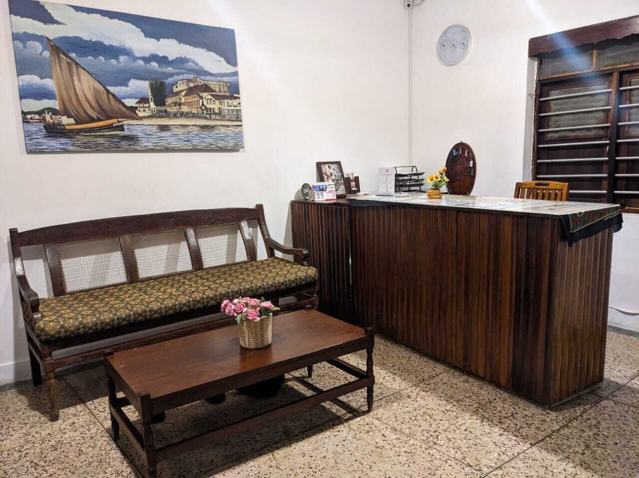 A room with a wooden bench, a small wooden table with a vase of flowers, a wooden counter, and a painting of a sailboat on the wall.