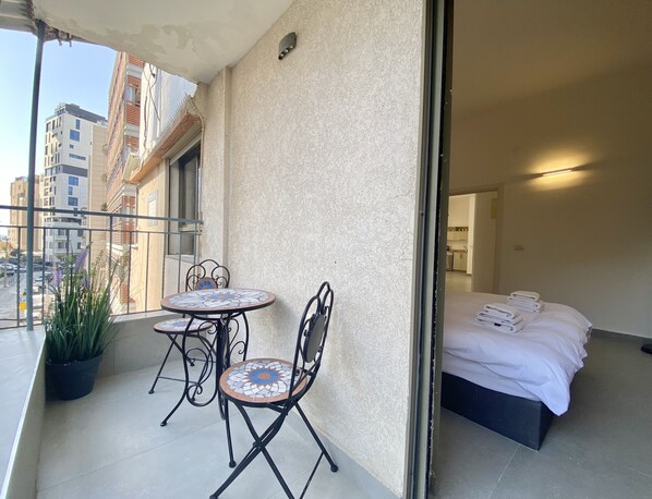 Een balkon met een kleine tafel en stoelen, een bloempot en een bed met keurig opgevouwen handdoeken.
