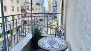Un balcone con un tavolo piastrellato, piante in vaso e vista su una strada trafficata con auto ed edifici.