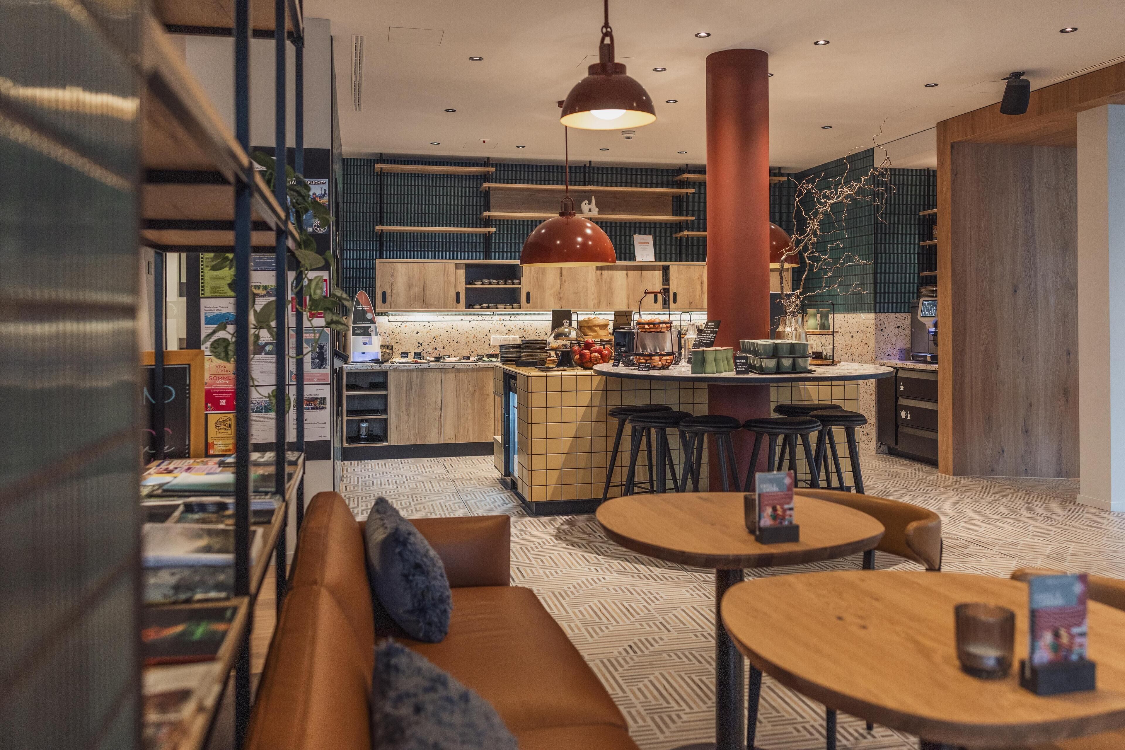 Un interior moderno con una cocina central, una zona de comedor con mesas redondas y un área de estar con sofá.