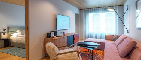 A modern hotel room with a wooden ceiling, a bed, a desk with a computer, a sofa, and a chair.