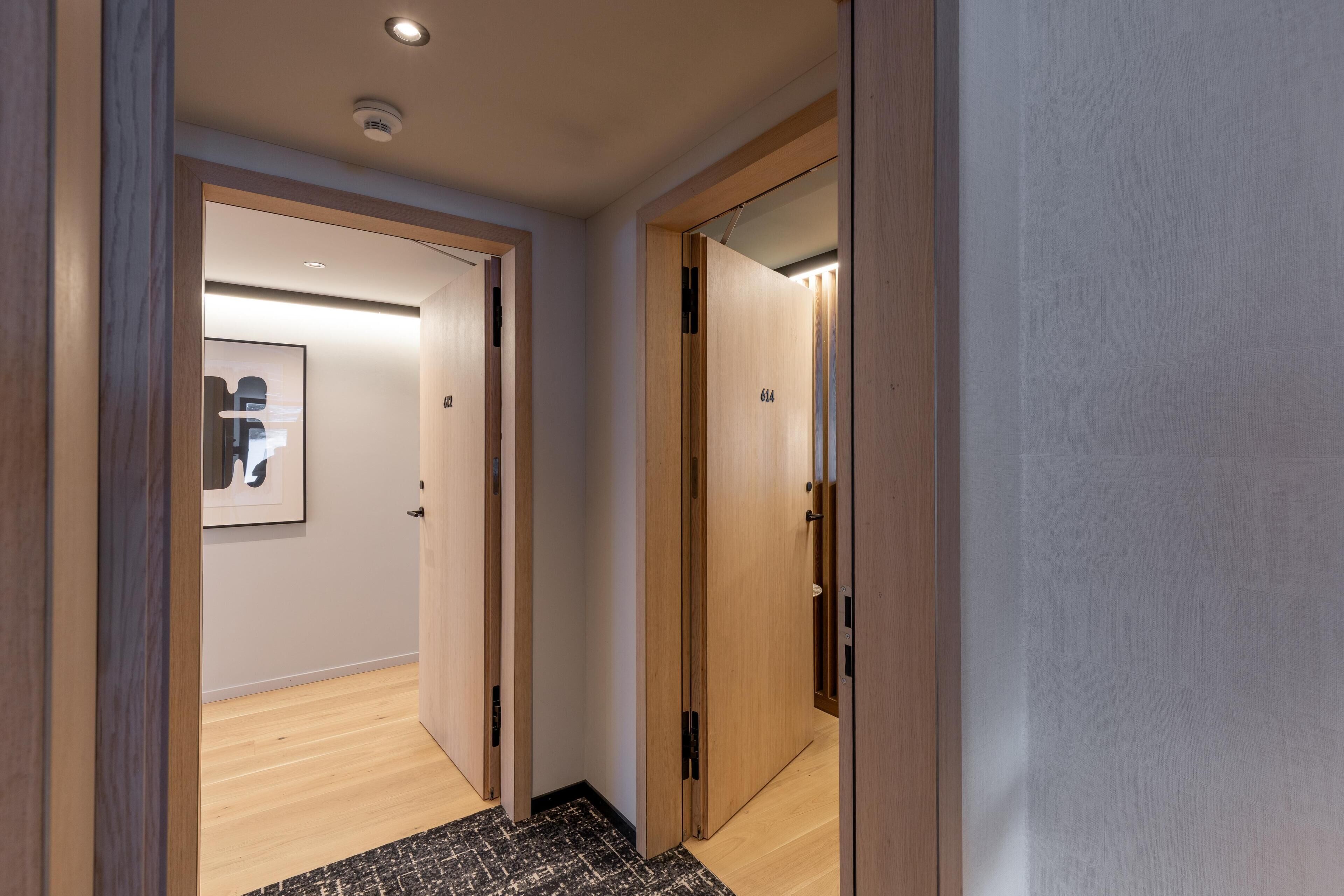 Un couloir avec des portes en bois, un tableau encadré au mur et un tapis à motifs.