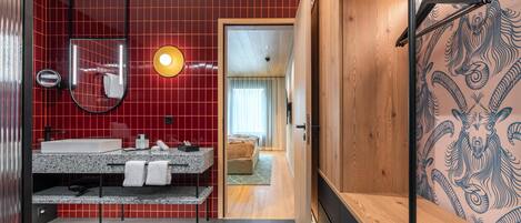 Un baño moderno con pared de azulejos rojos, tocador de madera, espejo y perchero.