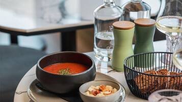 Una mesa de comedor con un tazón de sopa, un tazón de nueces, una cesta de pan, un vaso de agua y una copa de vino.