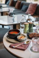 Una mesa de comedor con un tazón de sopa, un tazón de nueces, una cesta de pan, un vaso de agua y una copa de vino.