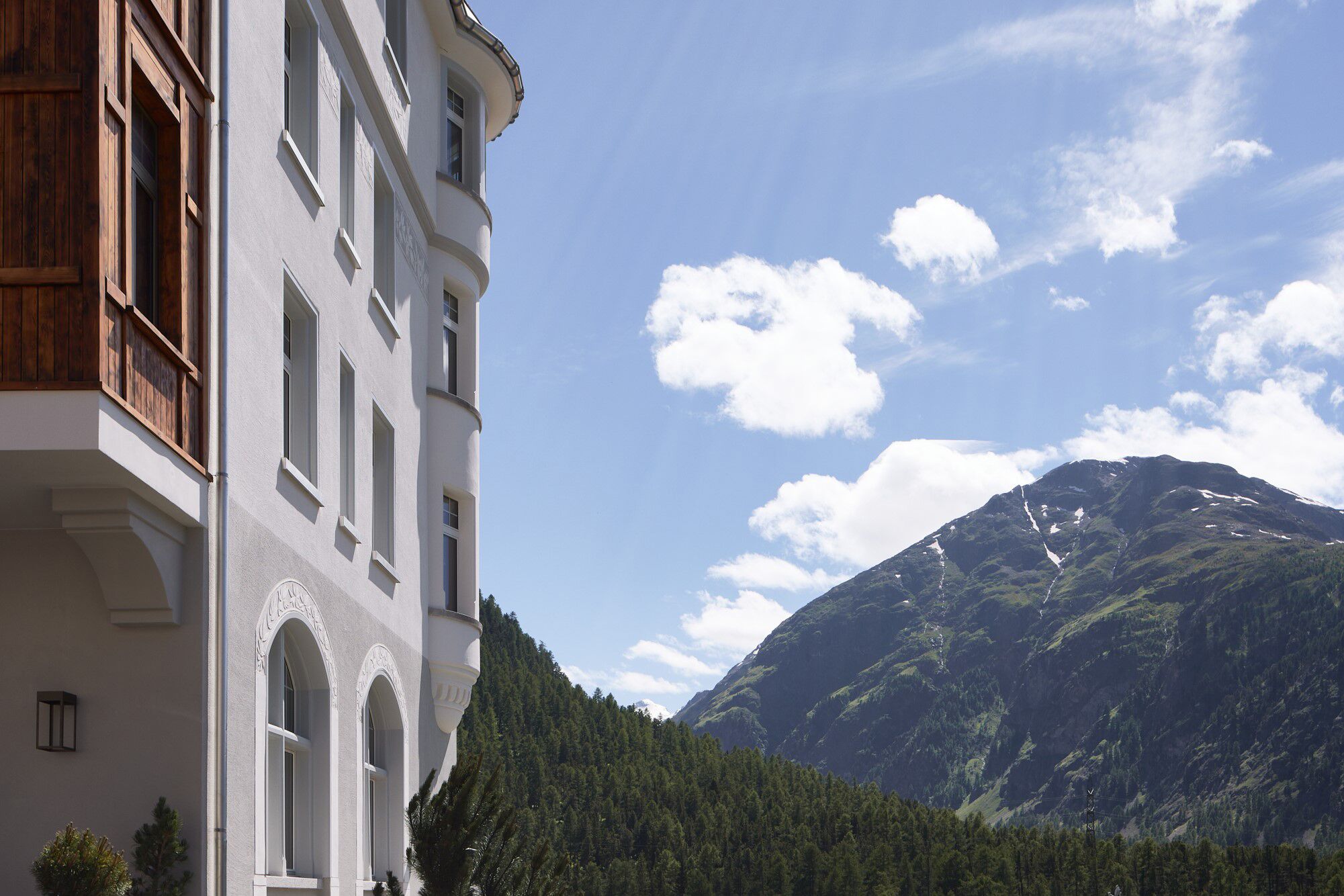 A building with arched windows and a balcony, set against a mountainous backdrop with a clear sky.