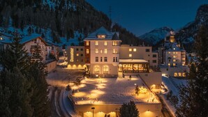 Um hotel grande, com vários andares e um pátio central, rodeado por montanhas cobertas de neve.