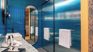 A modern bathroom with blue tiles, a large mirror, a sink with toiletries, and a glass shower enclosure.