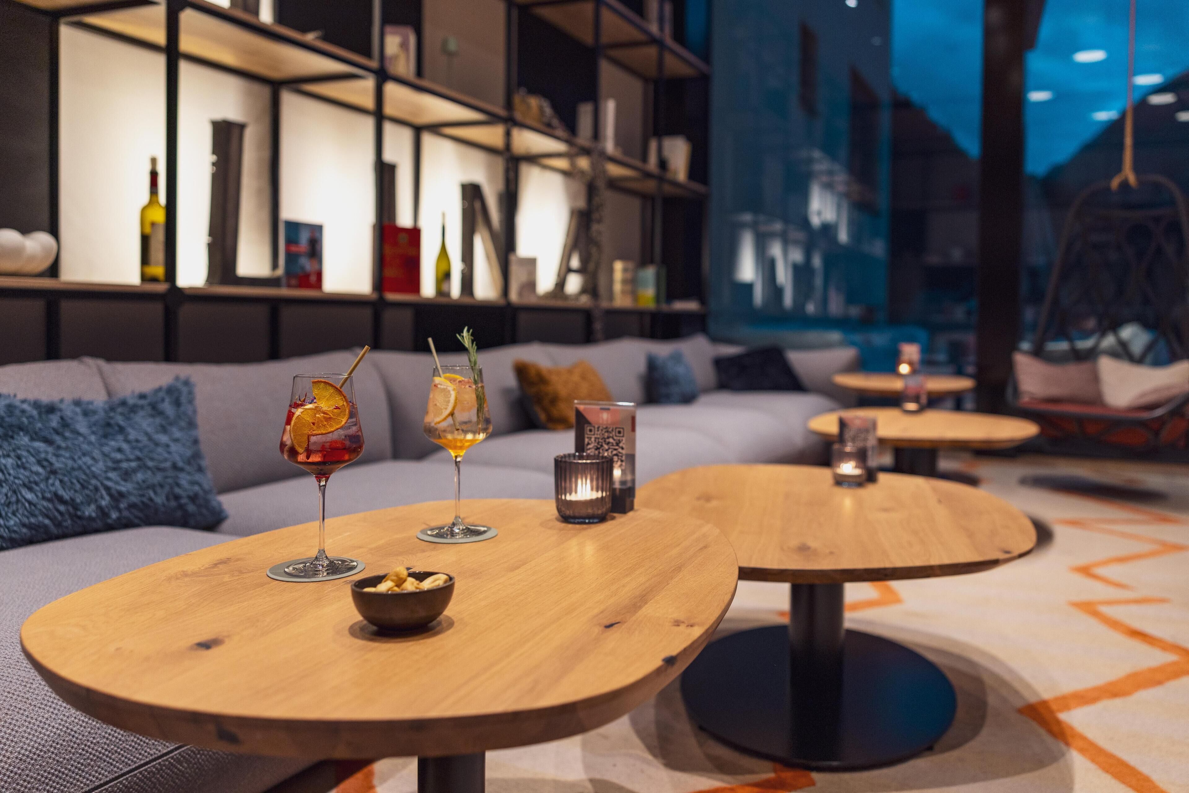 Un área de estar moderna con mesas redondas de madera, un sofá y una estantería.