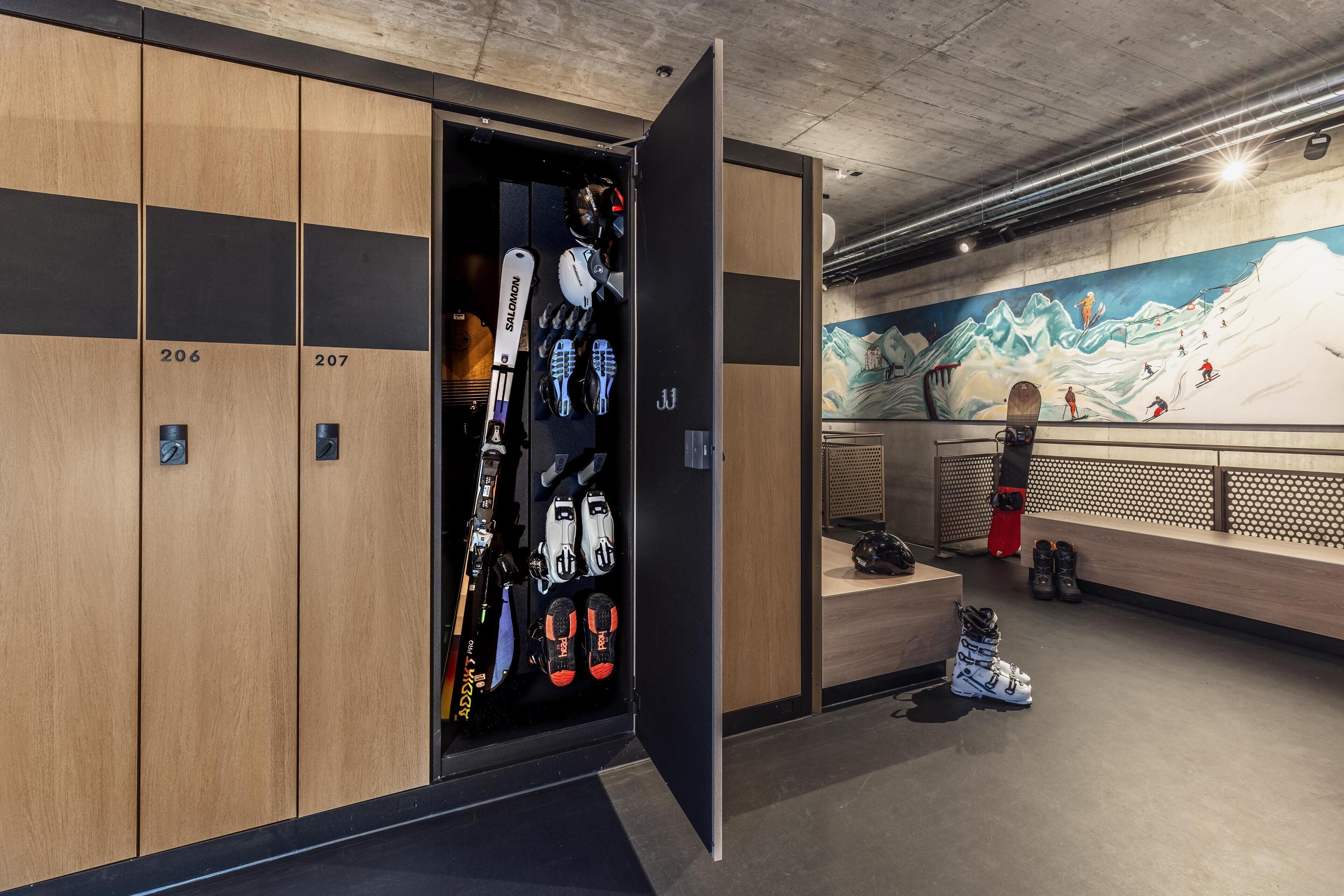 A ski locker room with numbered lockers, ski equipment, and a mural of a snowy mountain scene.