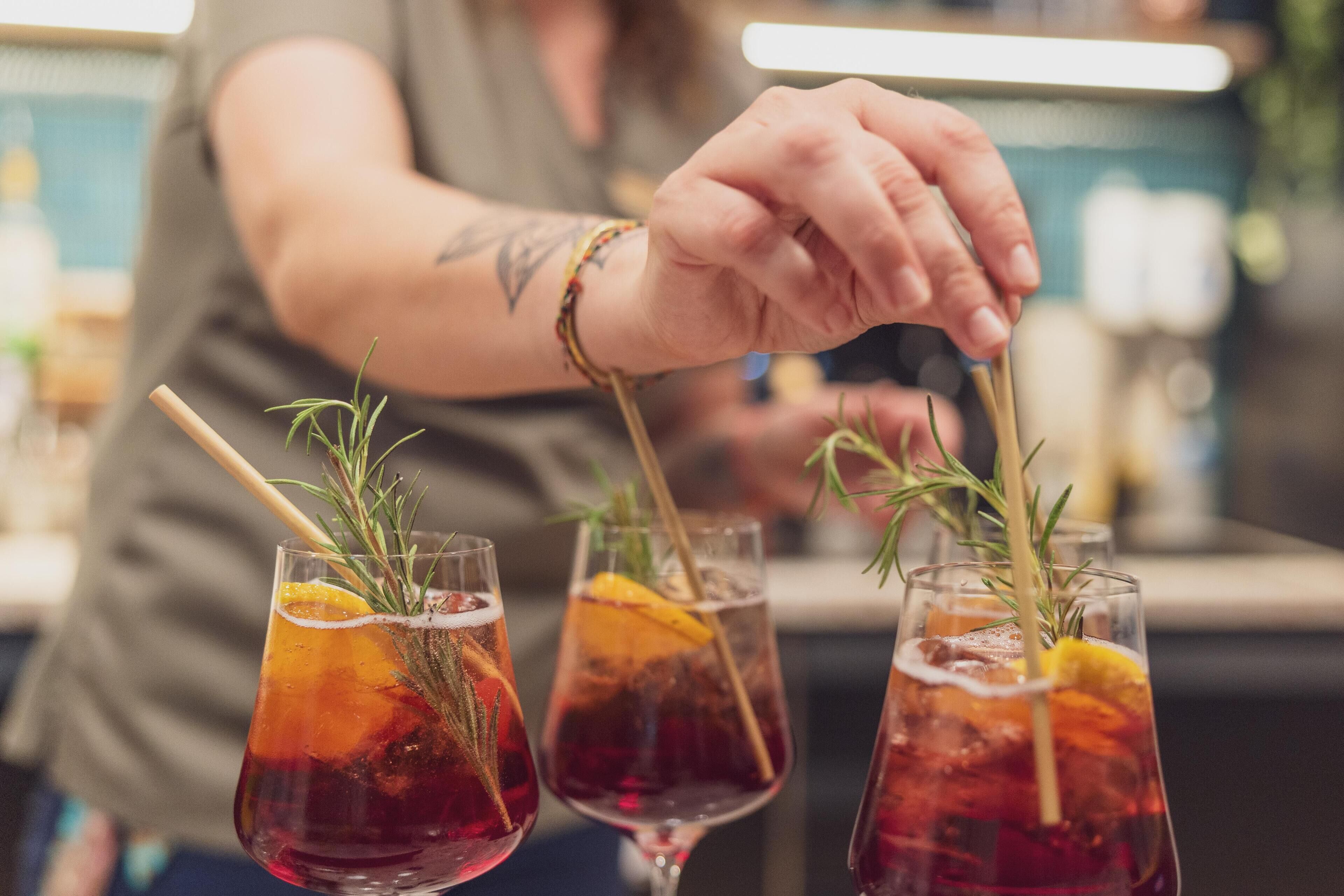 Una persona preparando bebidas con ramitas de romero en vasos.