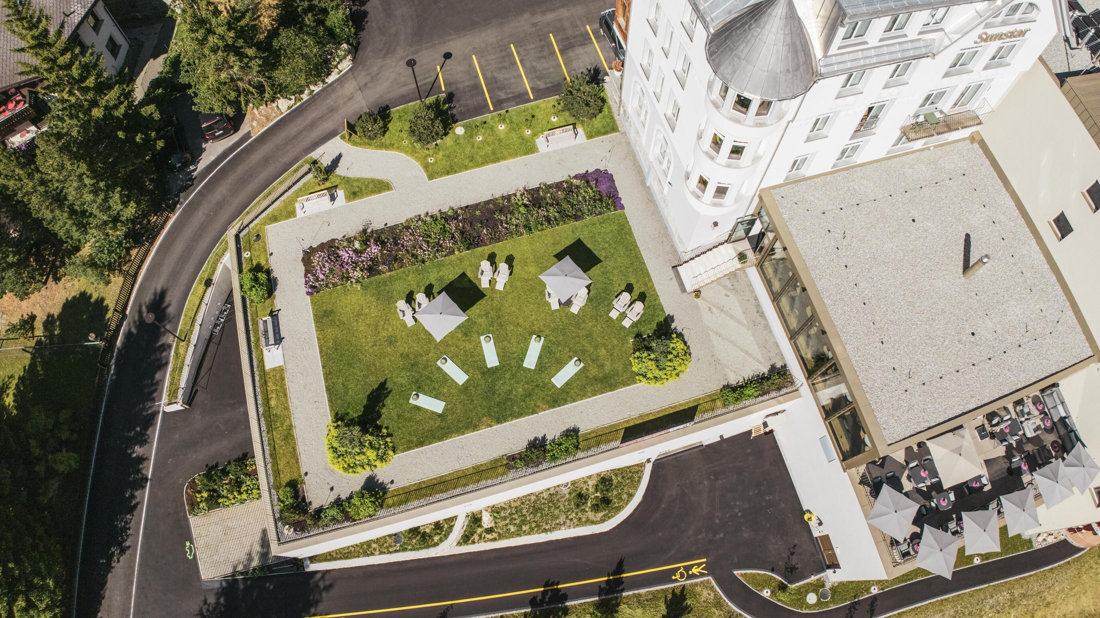 An aerial view of a hotel with a central courtyard featuring outdoor seating, a parking area, and a building with a dome and a sign reading "Sunstar."