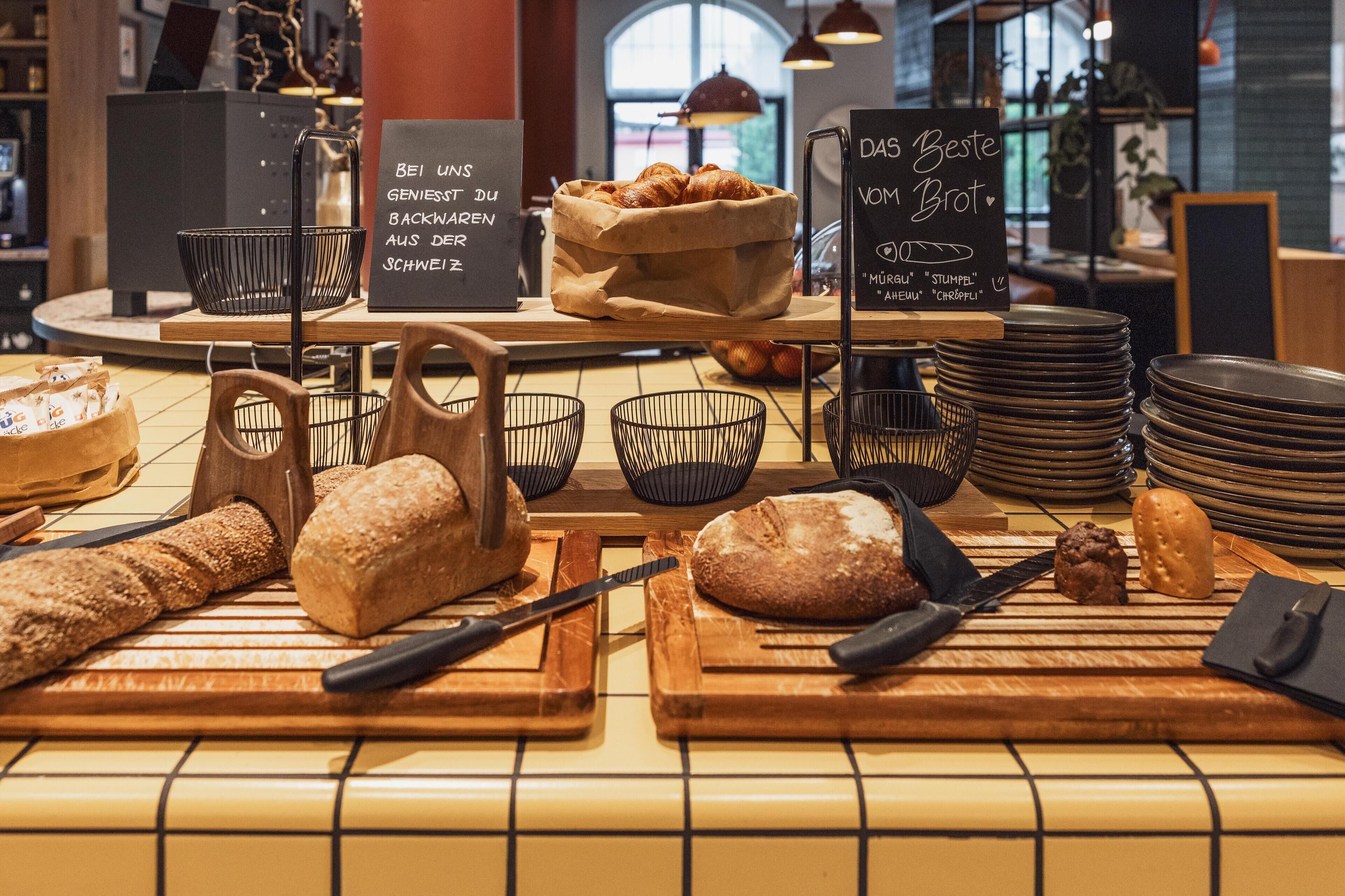 A bakery display with various breads and pastries, a sign with German text, and a stack of plates.
