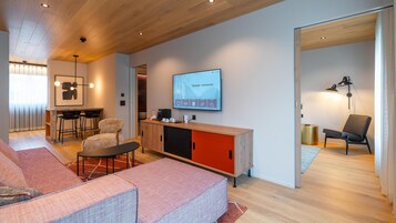 Una sala de estar moderna con un sofá, un comedor, un televisor mostrando 'Sunstar PONTRESINA' y una cocina.
