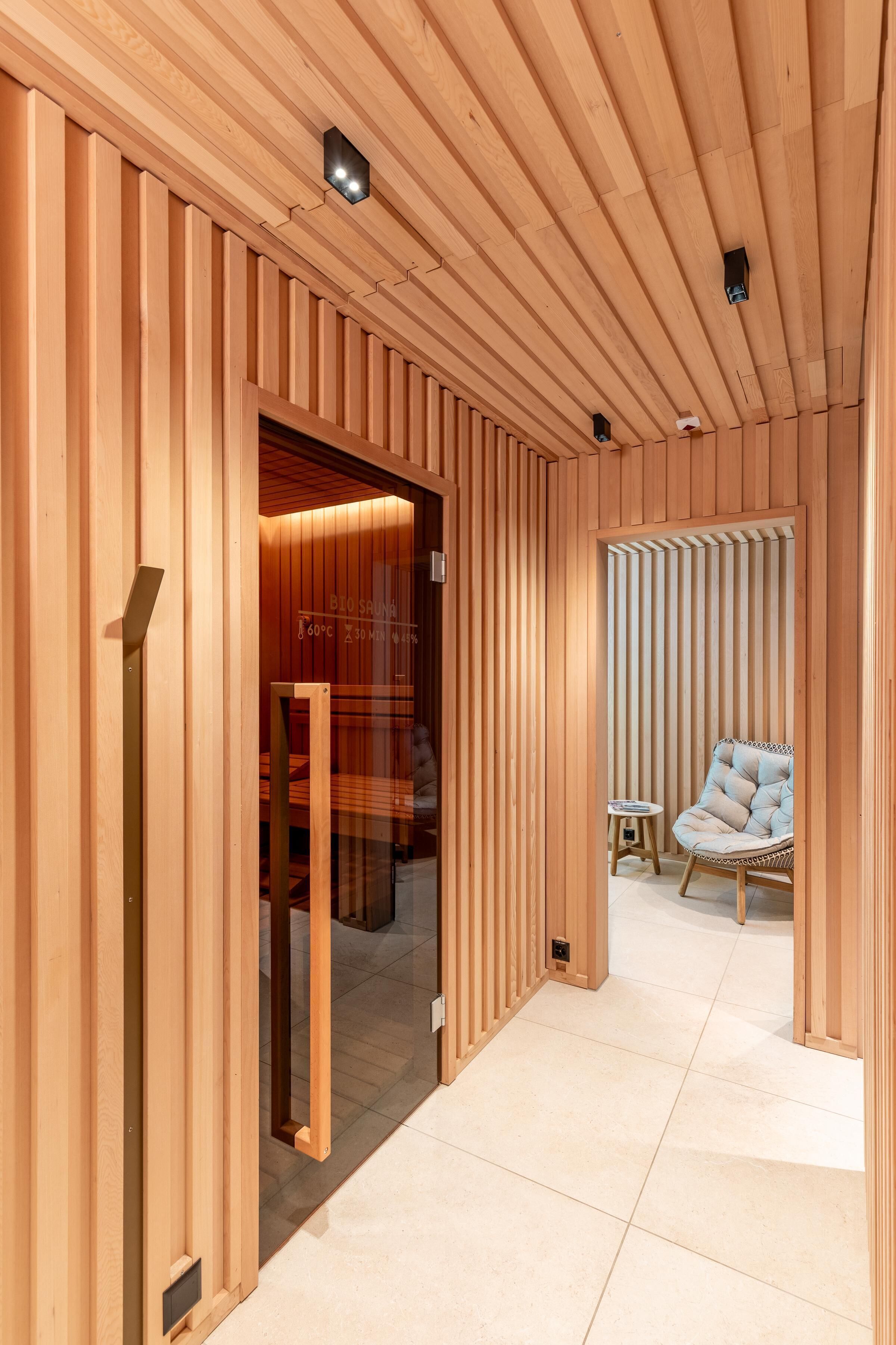 A corridor with wooden slats, a glass door leading to a room, and a wicker chair in the distance.