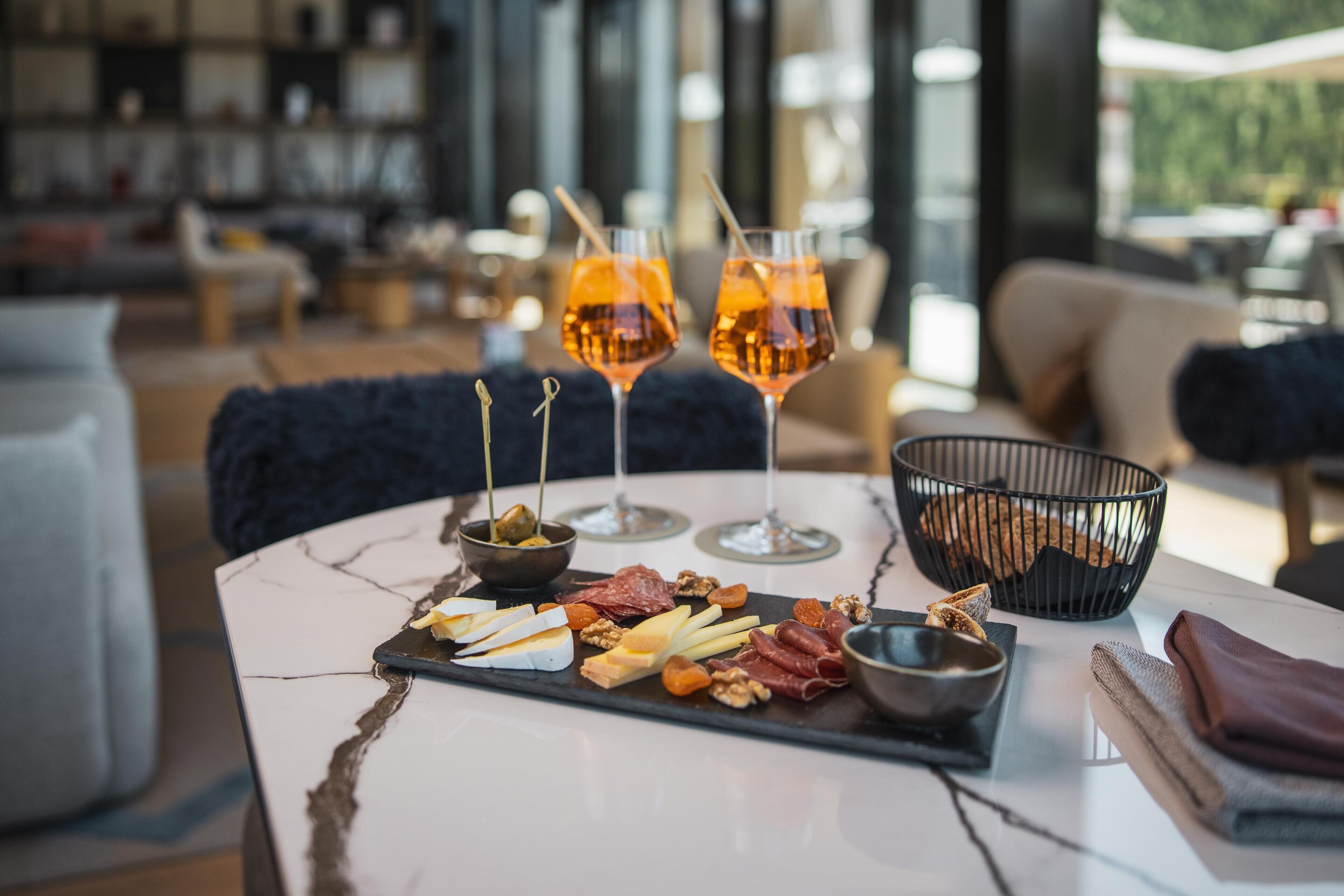 A table with a charcuterie board, glasses of orange drink, and a black bowl with bread.