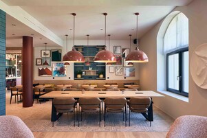 Un comedor moderno con una mesa larga y sillas, luces colgantes y vistas a la cocina al fondo.