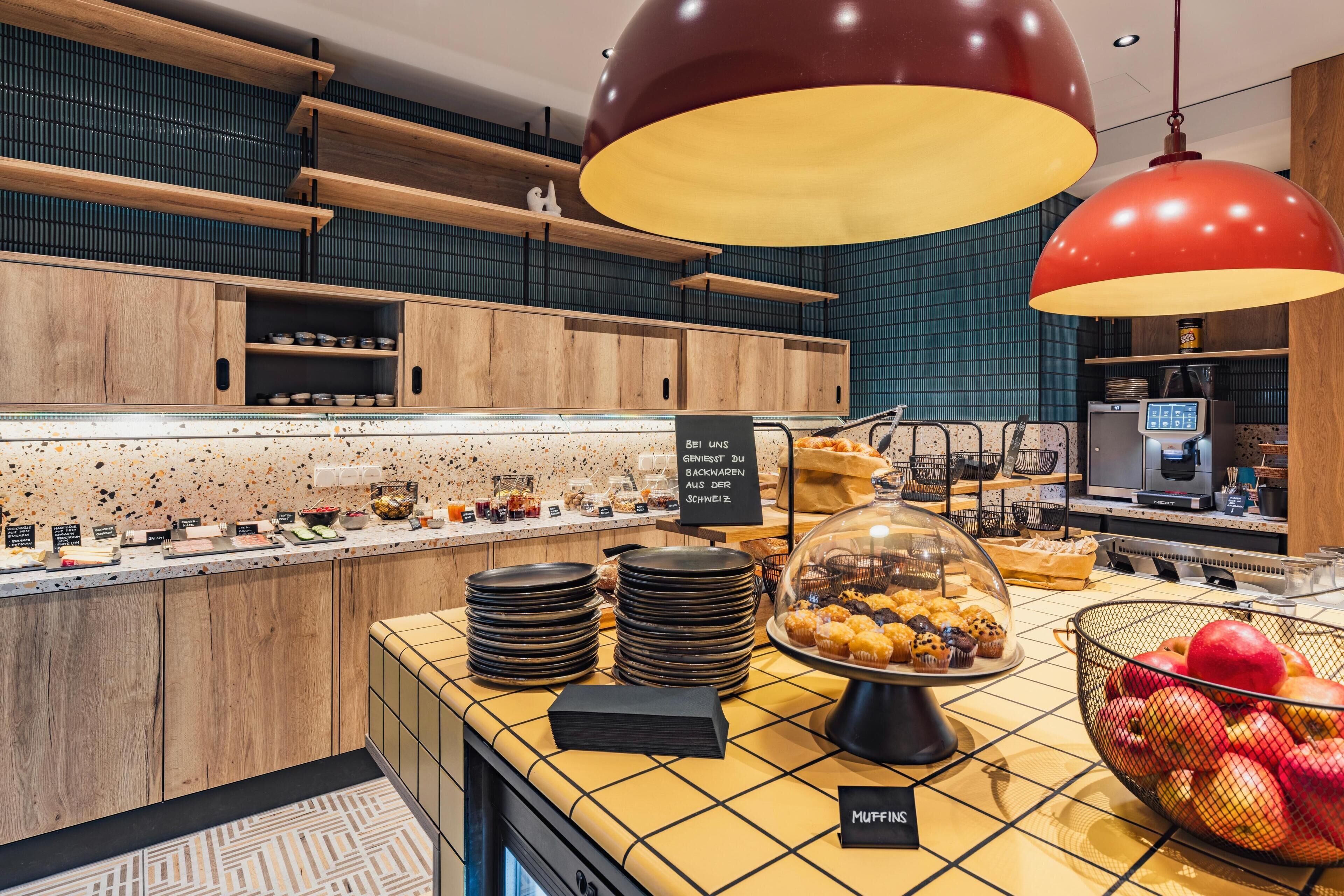 A bakery counter with muffin display, a fruit bowl, and a coffee machine.