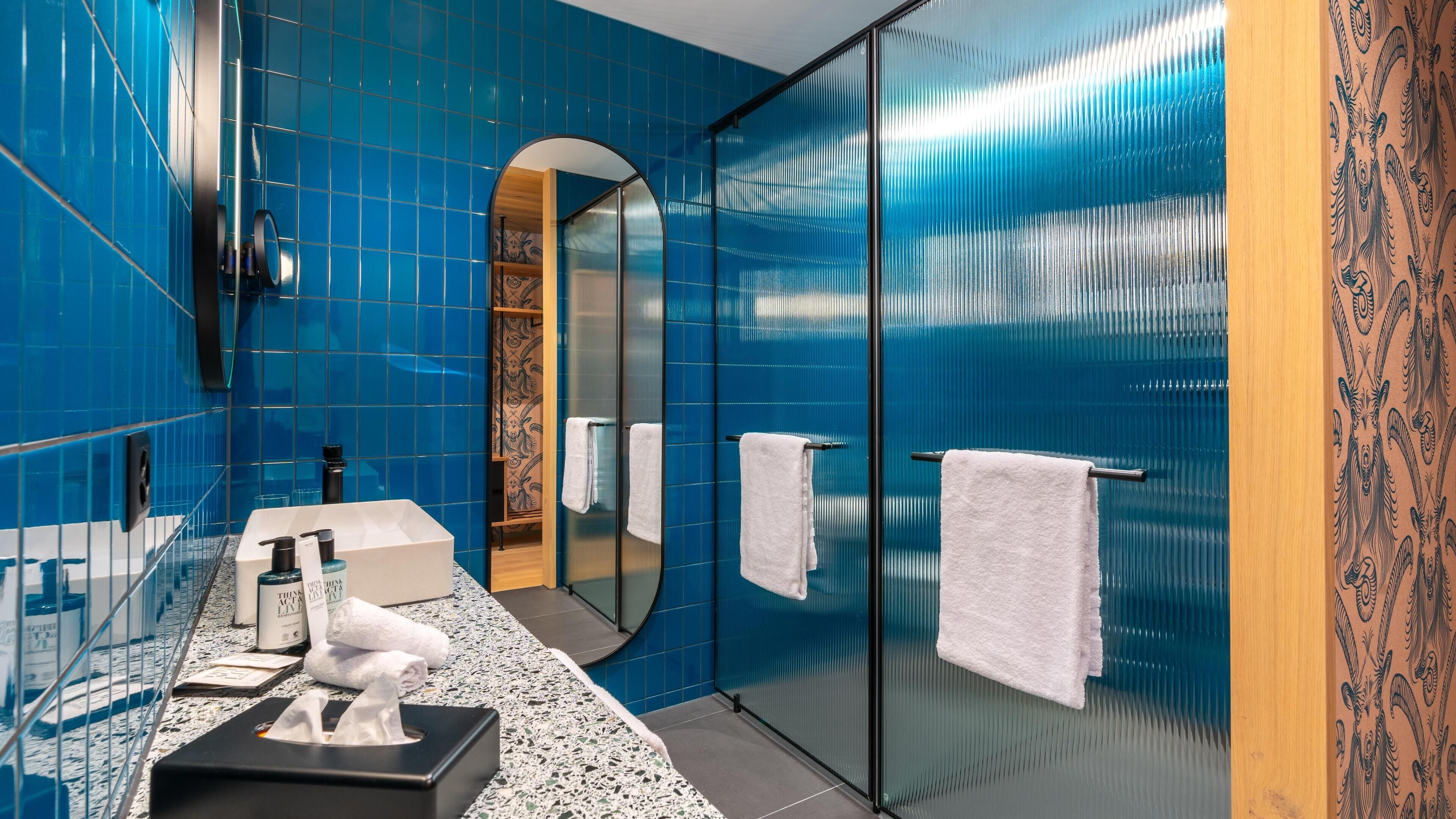 A bathroom with blue tiles, a glass shower enclosure, a vanity with a mirror, and a towel rack.