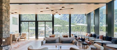 A spacious lounge area with a stone fireplace, comfortable seating, and large windows offering mountain views.