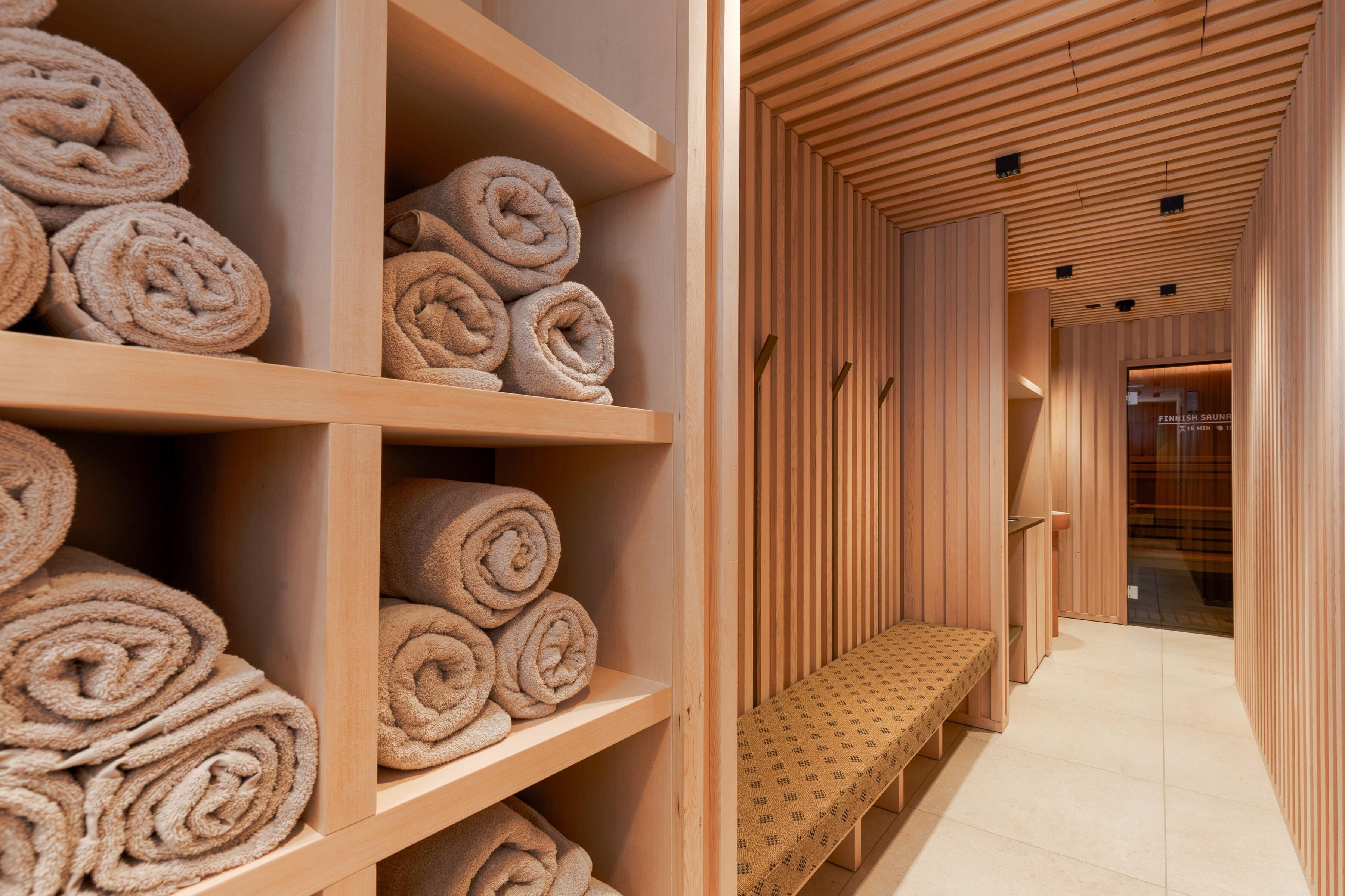 A wooden interior with shelves of rolled towels and a bench along a corridor.