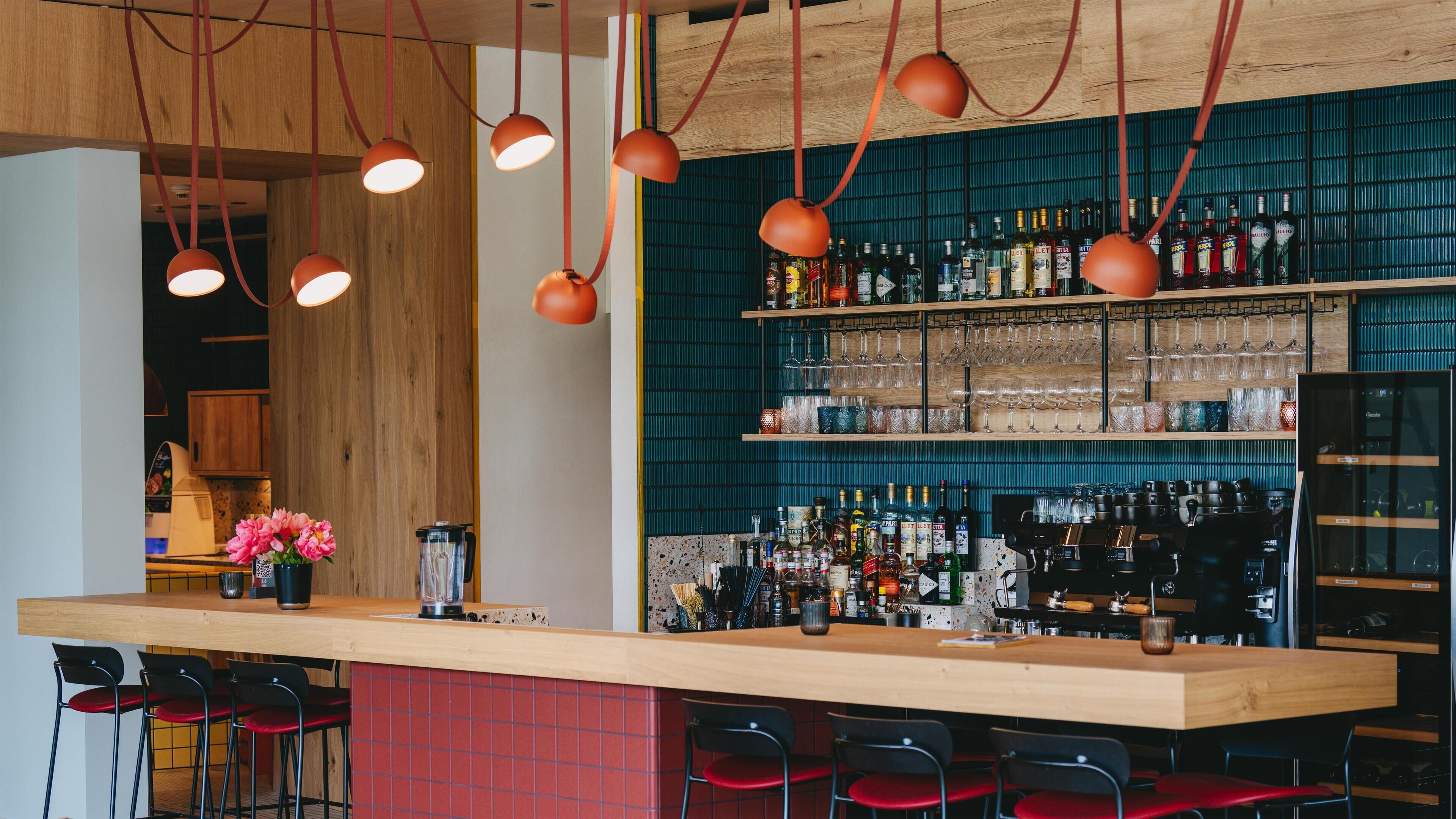 Eine Bar mit Holztresen, roten Stühlen und hängenden Pendelleuchten.