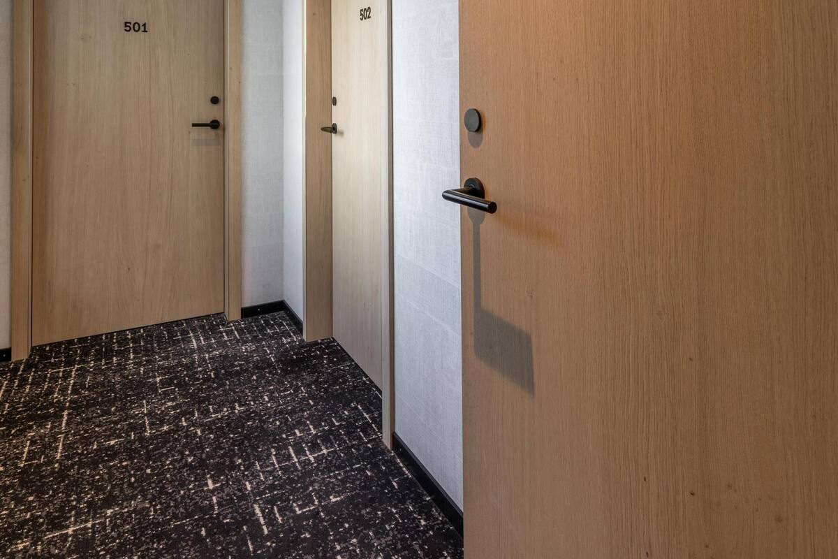 Ein Flur mit zwei Holztüren, die mit 501 und 502 beschriftet sind, einem schwarz-weißen gepunkteten Boden und einer weißen Decke mit eingelassener Beleuchtung.