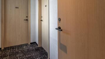 Um corredor com duas portas de madeira identificadas com os números 501 e 502, um chão com padrão preto e branco marmorizado e teto branco com iluminação embutida.