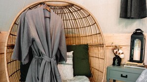 A room with a round wicker chair, a fluffy white stool, a small wooden nightstand, and a bed with a white cover. - Goat Farm Tree House on Creek (Newport)