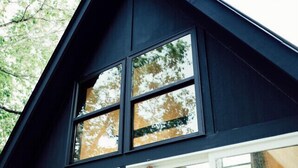 A modern house with a large window and a robe hanging in front. - Goat Farm Tree House on Creek (Newport)