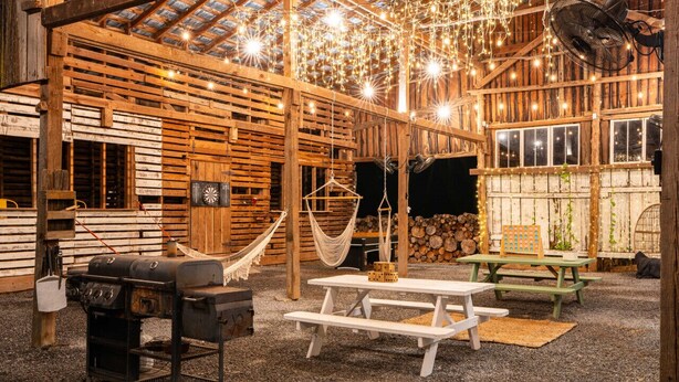 A rustic wooden interior with a high ceiling, wooden beams, a hammock, picnic tables, and a grill. - Goat Farm Tree House on Creek (Newport)