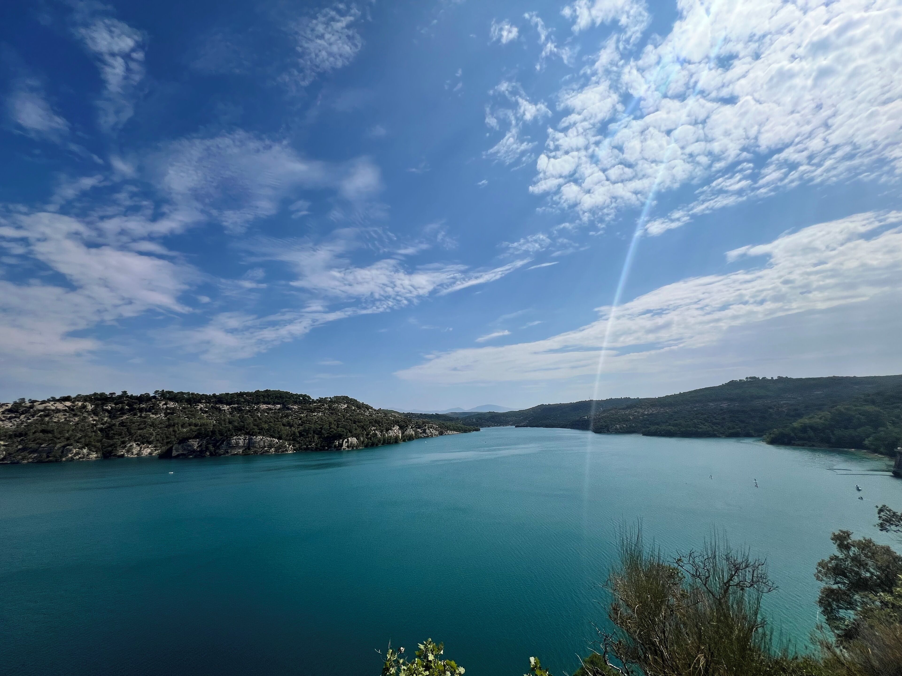 A panoramic view of a calm lake surrounded by hills with sparse vegetation, under a partly cloudy sky.