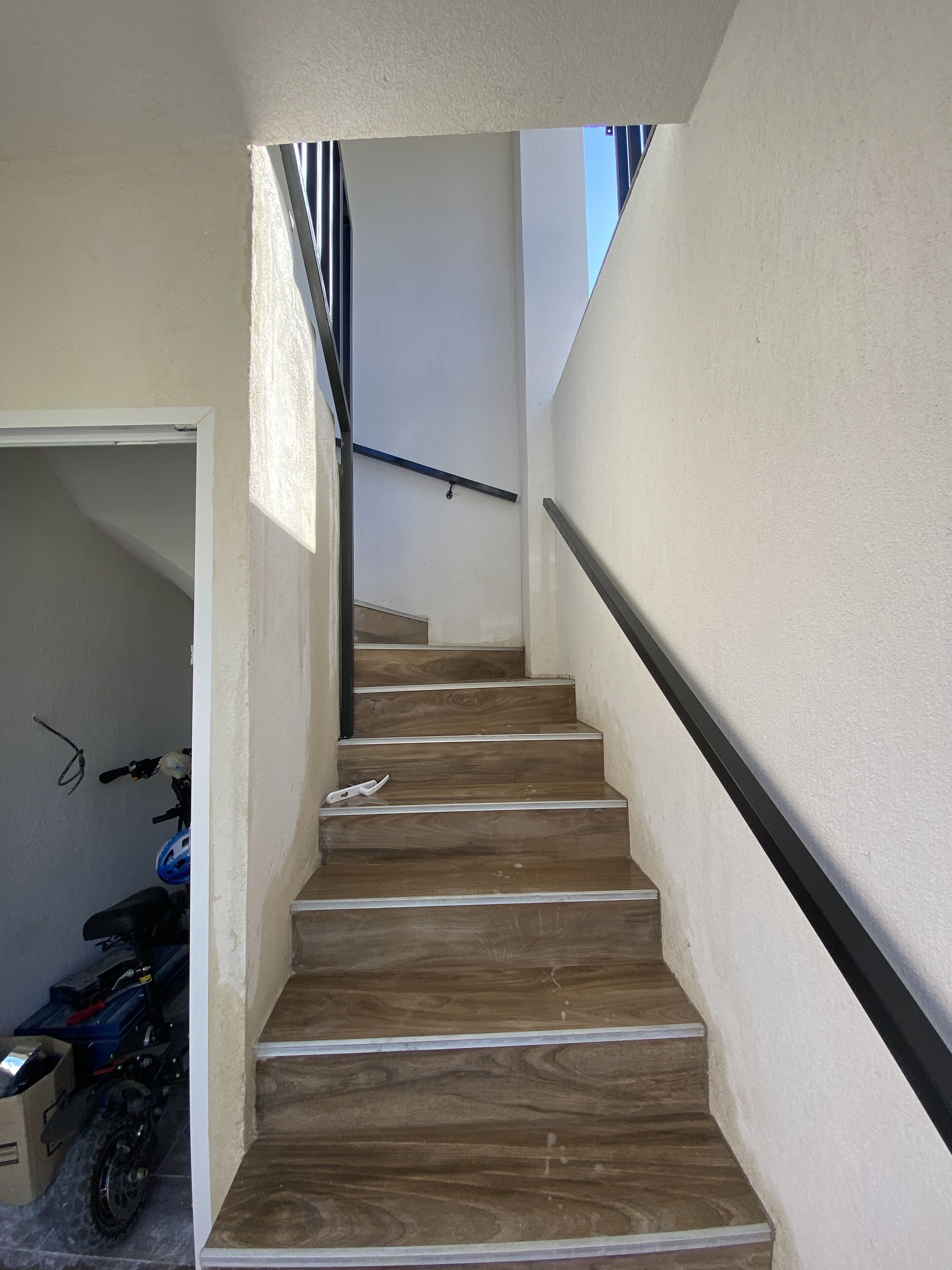 Eine Treppe mit Holzbodenstufen und einem schwarzen Geländer, die zu einer Zwischenebene mit einem Metallgeländer führt.