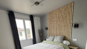 Ein modernes Schlafzimmer mit einem großen Bett, einem Deckenventilator, einer Wandverkleidung aus Holzleisten und einem kleinen Nachttisch.