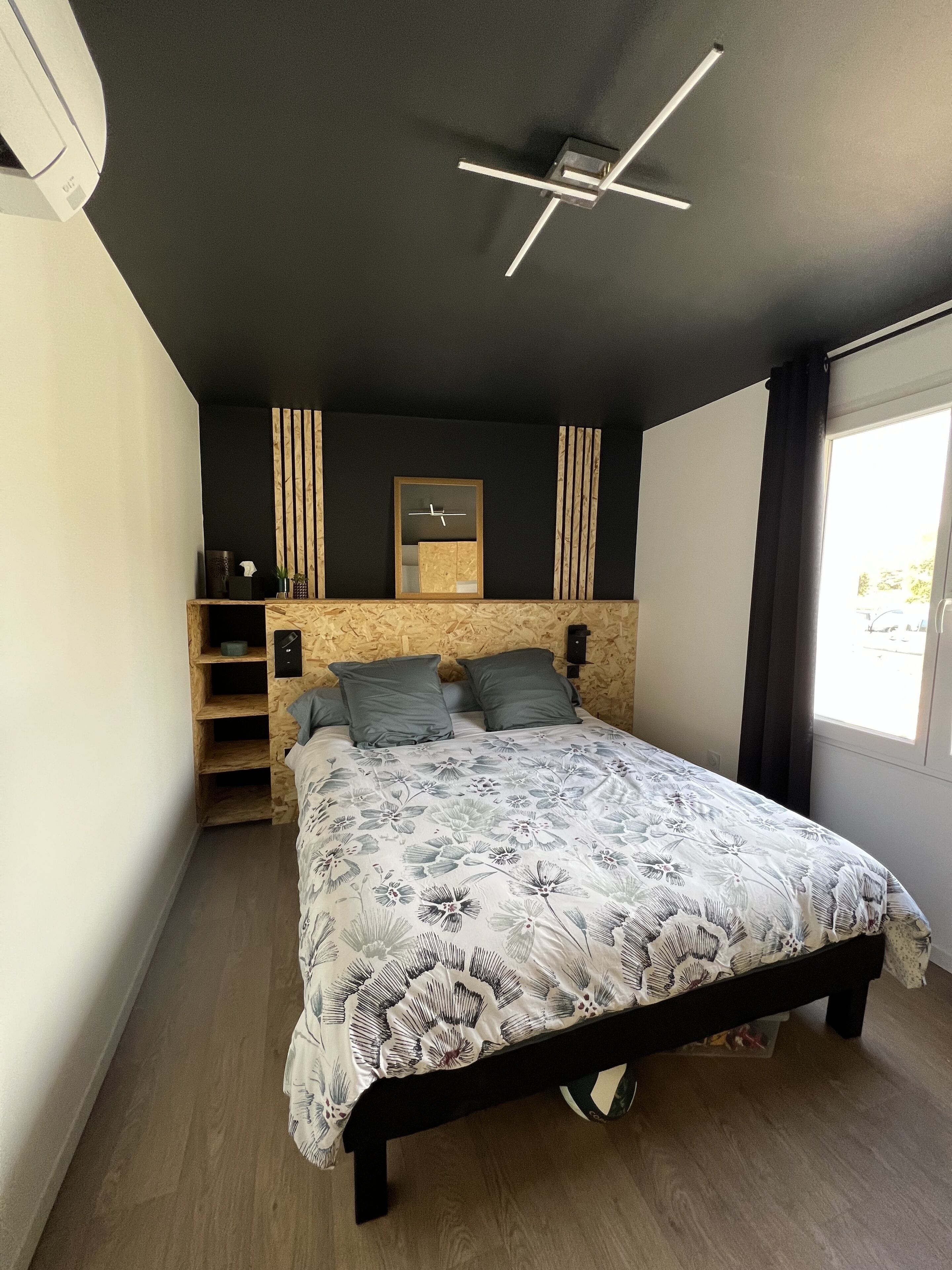Ein modernes Schlafzimmer mit Bett, Einbauschränken, Deckenventilator und Fenster mit Vorhängen.