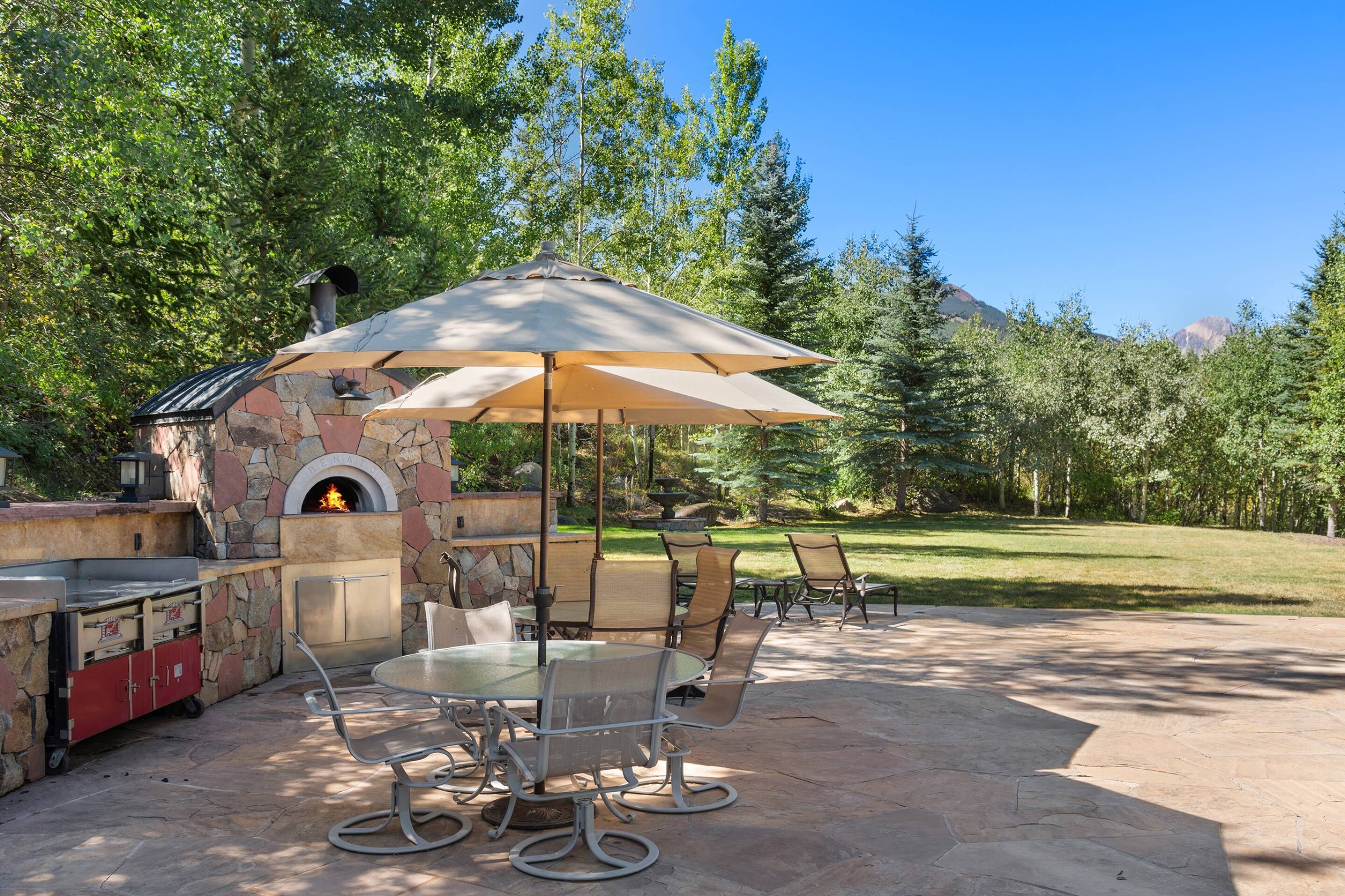 Une terrasse extérieure avec une cheminée en pierre, une table ronde et des chaises.