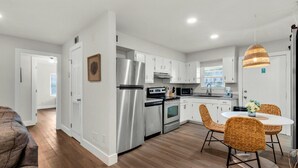 Una cucina moderna con elettrodomestici in acciaio inossidabile, mobili bianchi e un'area pranzo con sedie in vimini.