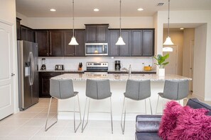 A modern kitchen with dark cabinets, a stainless steel refrigerator, a microwave, a stove, and four bar stools. - Resort Home With Pool-Sleeps 14 Free Wifi /Parking (Four Corners)
