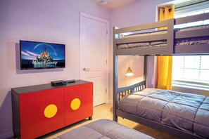 A room with a bunk bed, a TV mounted on the wall, a red cabinet with yellow circles, and a window with curtains.