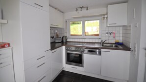 Una cucina compatta con mobili bianchi, forno integrato, lavastoviglie e una finestra che offre luce naturale.