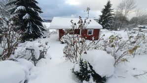 Paesaggio innevato con una piccola baita rossa e un grande abete sempreverde.